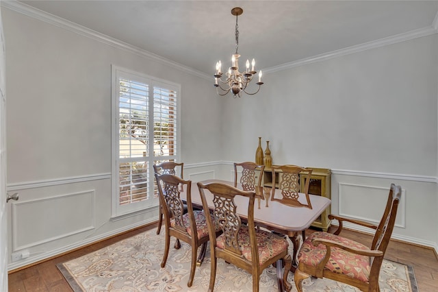 dining space with a chandelier, wood-type flooring, a wainscoted wall, and crown molding