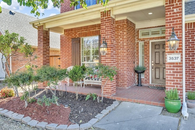 entrance to property featuring a porch and brick siding