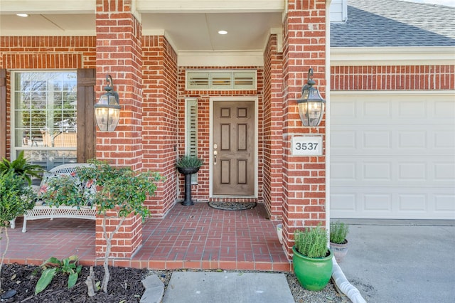 property entrance with a garage, brick siding, and roof with shingles