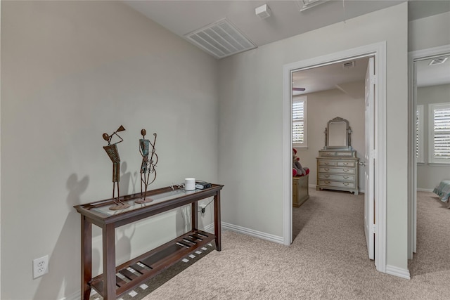 hall featuring attic access, light colored carpet, a healthy amount of sunlight, and visible vents