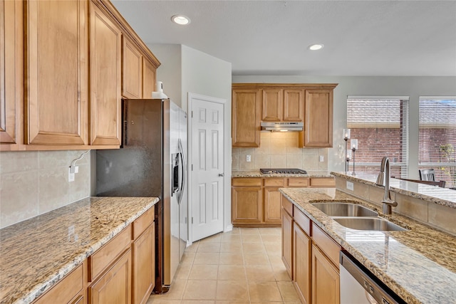 kitchen with light tile patterned floors, light stone counters, under cabinet range hood, stainless steel appliances, and a sink