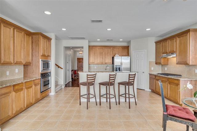 kitchen with visible vents, an island with sink, a breakfast bar, stainless steel appliances, and under cabinet range hood