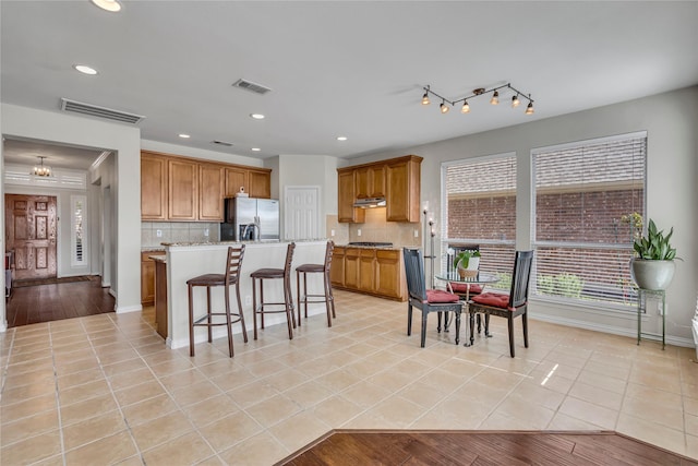 kitchen featuring visible vents, stainless steel refrigerator with ice dispenser, brown cabinets, a center island, and tasteful backsplash