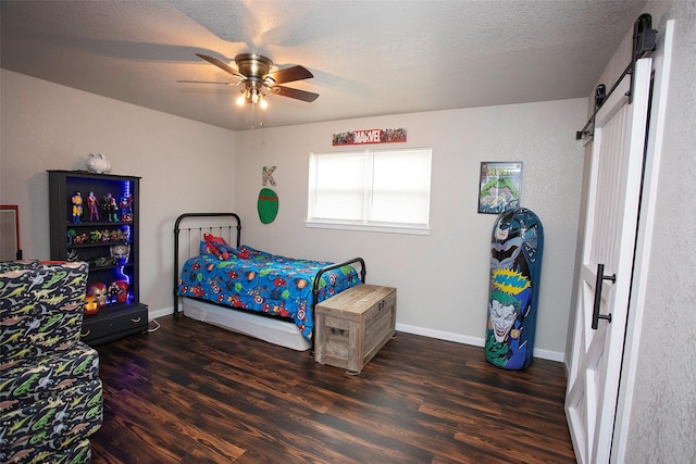 bedroom featuring a barn door, ceiling fan, a textured ceiling, wood finished floors, and baseboards