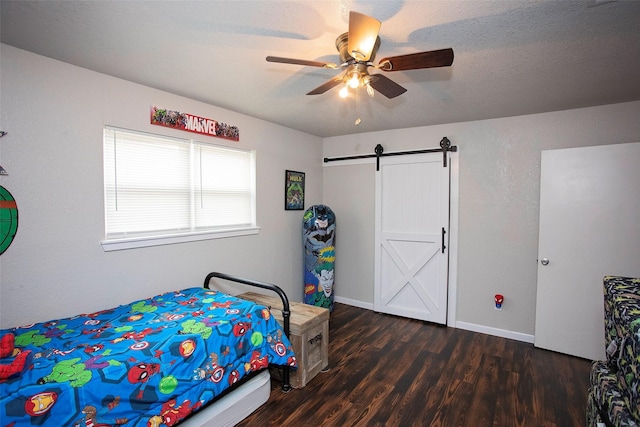 bedroom with ceiling fan, a textured ceiling, a barn door, dark wood-type flooring, and baseboards