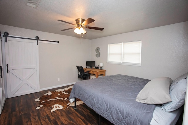 bedroom with a textured ceiling, a barn door, wood finished floors, visible vents, and baseboards