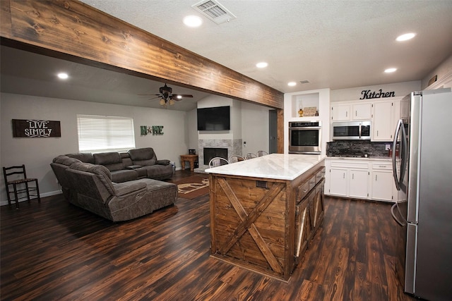 kitchen featuring open floor plan, stainless steel appliances, a fireplace, and white cabinets