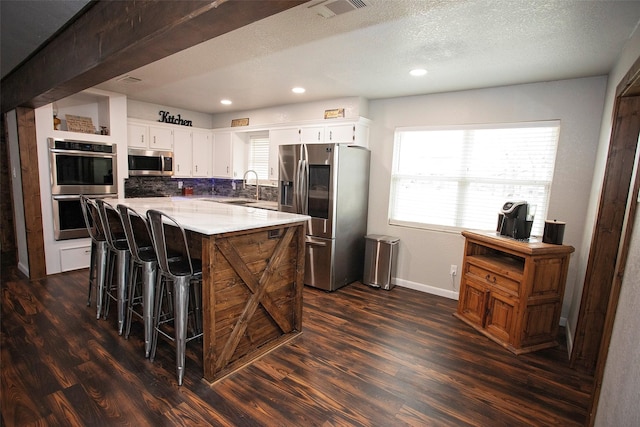 kitchen with stainless steel appliances, a sink, visible vents, light countertops, and dark wood finished floors