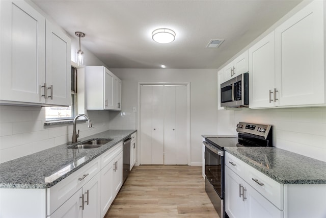 kitchen featuring stone countertops, stainless steel appliances, a sink, visible vents, and light wood finished floors