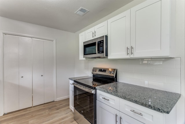 kitchen featuring visible vents, decorative backsplash, dark stone countertops, stainless steel appliances, and light wood-style floors