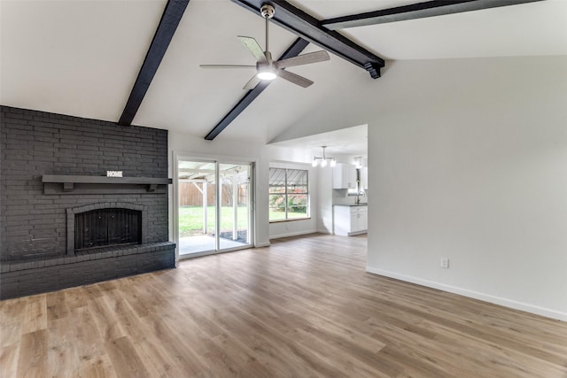 unfurnished living room featuring ceiling fan with notable chandelier, light wood-type flooring, a brick fireplace, and vaulted ceiling with beams