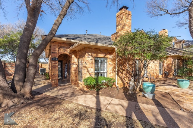 back of property with a patio area, a shingled roof, a chimney, and brick siding