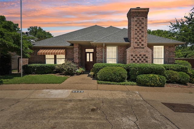 view of front of house featuring a shingled roof, fence, and brick siding