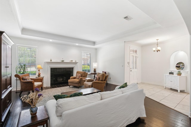 living area featuring a tray ceiling, visible vents, a tiled fireplace, baseboards, and hardwood / wood-style flooring