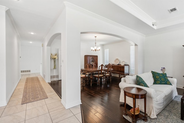 living area featuring light wood-style flooring, visible vents, arched walkways, and ornamental molding