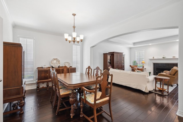 dining room featuring arched walkways, a tile fireplace, dark wood-style floors, ornamental molding, and an inviting chandelier