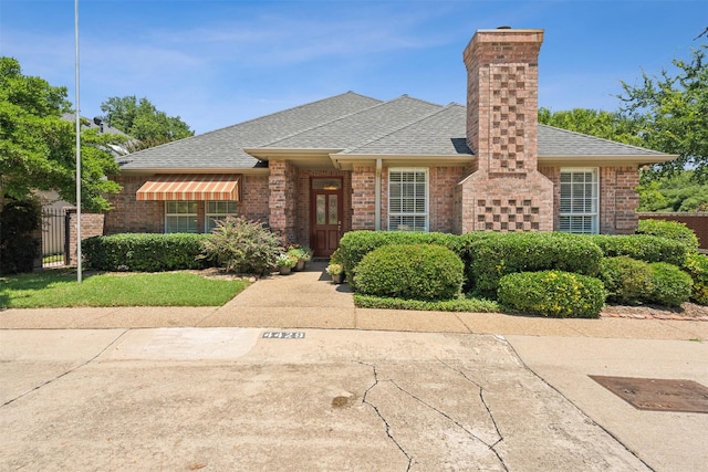 view of front of property featuring roof with shingles, fence, and brick siding