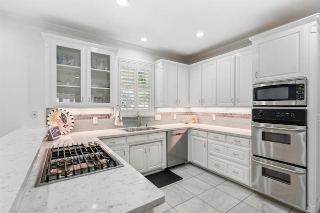 kitchen featuring decorative backsplash, glass insert cabinets, appliances with stainless steel finishes, white cabinetry, and a sink