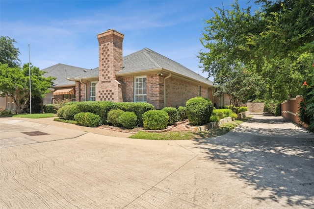 view of property exterior featuring roof with shingles, brick siding, a chimney, and fence