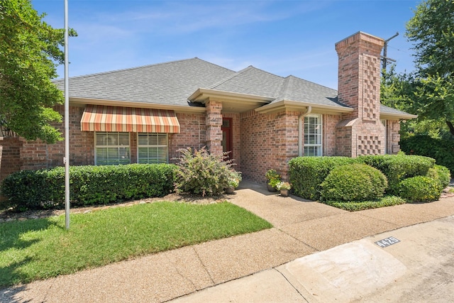 view of front of property with brick siding, a chimney, a shingled roof, and a front yard