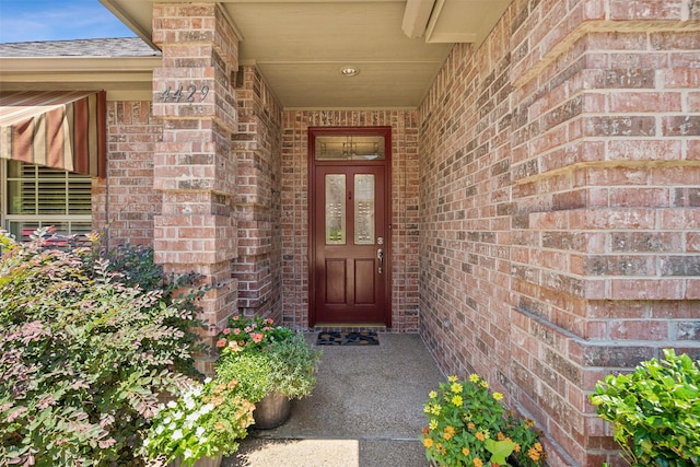 doorway to property featuring brick siding and roof with shingles