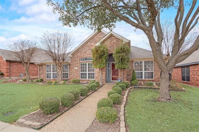 traditional home with a shingled roof, a front yard, and brick siding