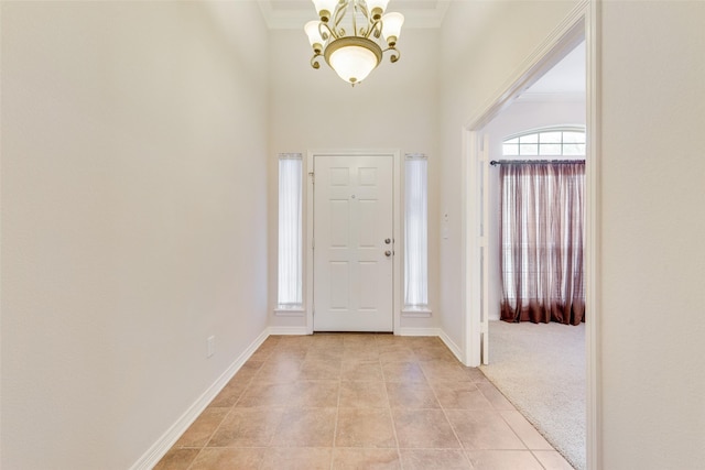 entryway with light tile patterned floors, a high ceiling, ornamental molding, a chandelier, and baseboards