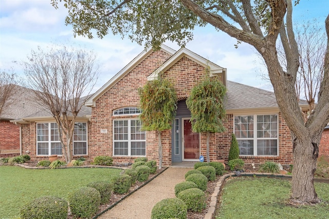 view of front of house featuring brick siding, a front lawn, and a shingled roof