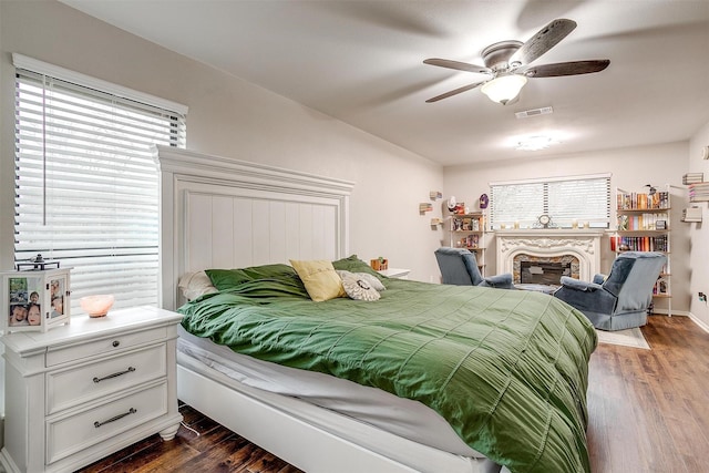 bedroom with a fireplace, visible vents, dark wood finished floors, and a ceiling fan