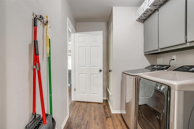 clothes washing area featuring dark wood-style flooring, cabinet space, washer and clothes dryer, and baseboards