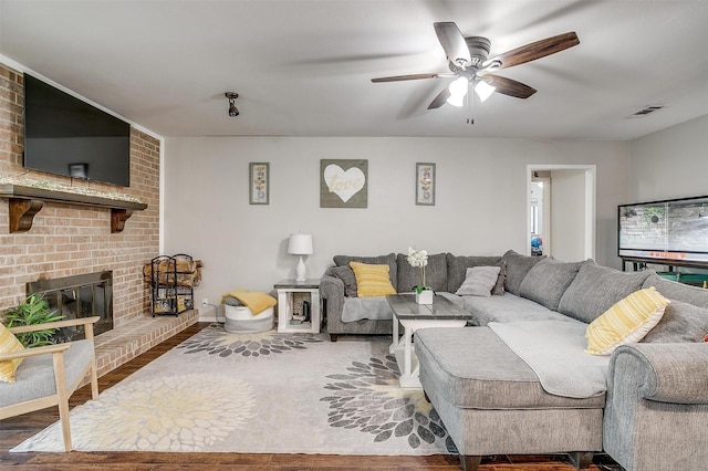 living room with visible vents, a ceiling fan, a brick fireplace, wood finished floors, and baseboards