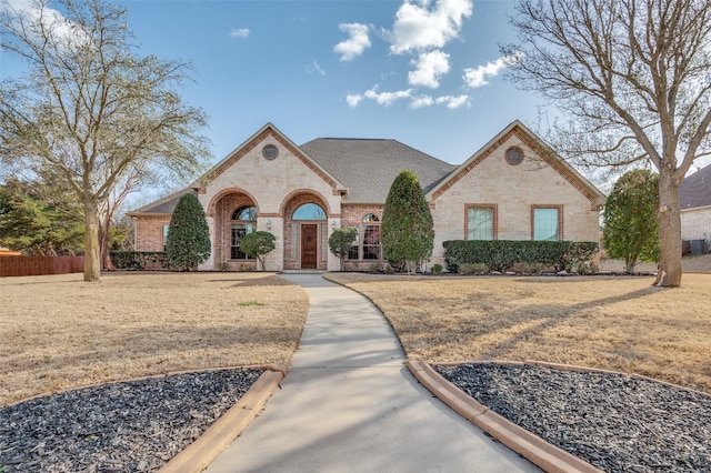 french country style house with brick siding, fence, and roof with shingles