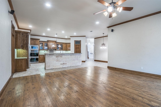 kitchen featuring ceiling fan with notable chandelier, a sink, brown cabinets, light wood finished floors, and stainless steel microwave