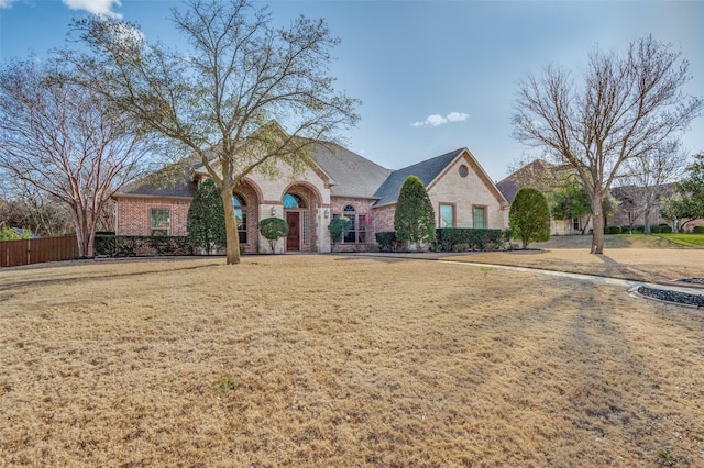 french provincial home with brick siding, a front yard, and fence