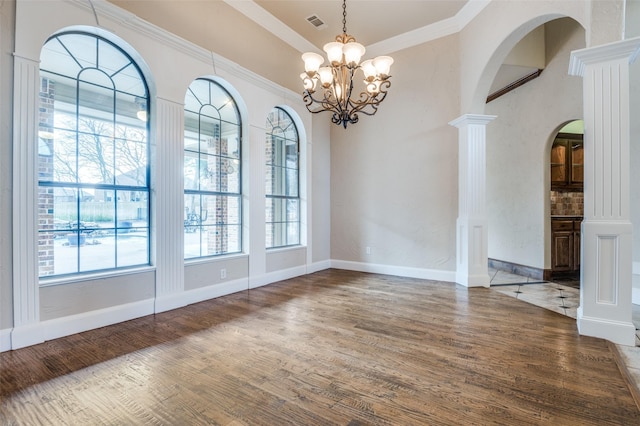 unfurnished room with arched walkways, ornamental molding, wood finished floors, and decorative columns