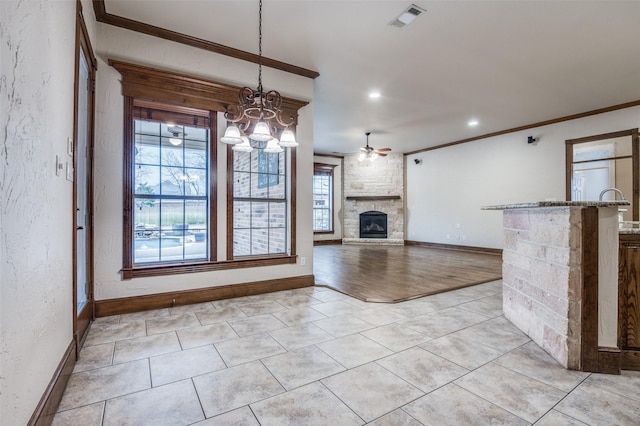 unfurnished living room with ceiling fan, a stone fireplace, visible vents, baseboards, and ornamental molding