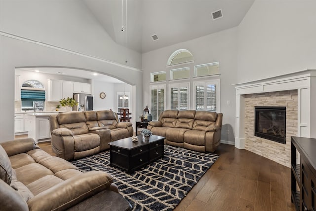 living room with dark wood-type flooring, arched walkways, visible vents, and a fireplace