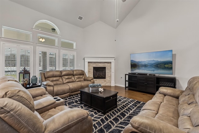 living room featuring high vaulted ceiling, a fireplace, wood finished floors, and visible vents