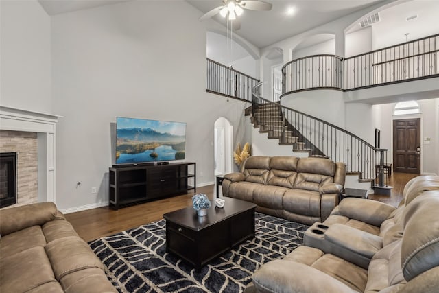 living area featuring baseboards, arched walkways, wood finished floors, stairs, and a fireplace