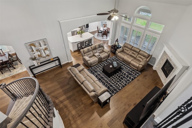 living area featuring baseboards, a ceiling fan, a glass covered fireplace, wood finished floors, and a high ceiling