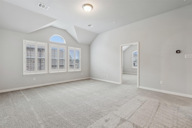 carpeted spare room with baseboards, visible vents, and vaulted ceiling