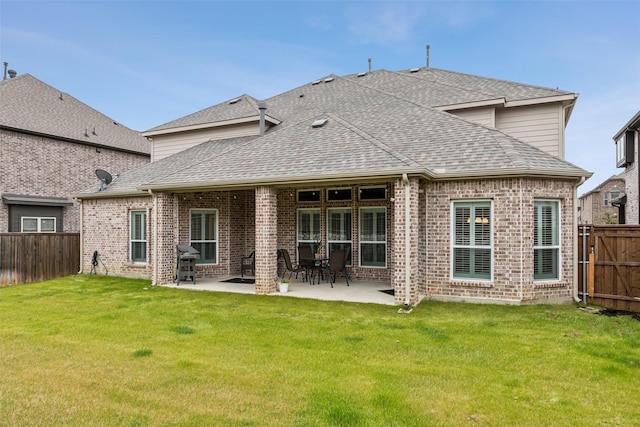 rear view of property featuring a shingled roof, a fenced backyard, a yard, a patio area, and brick siding