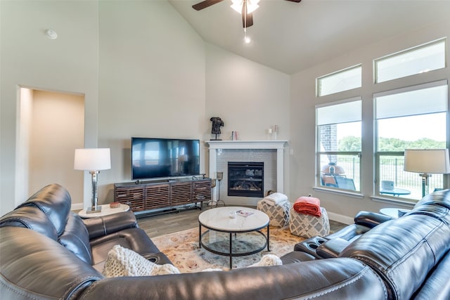 living room with a glass covered fireplace, ceiling fan, wood finished floors, high vaulted ceiling, and baseboards