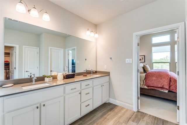 full bathroom with baseboards, a sink, ensuite bath, and double vanity