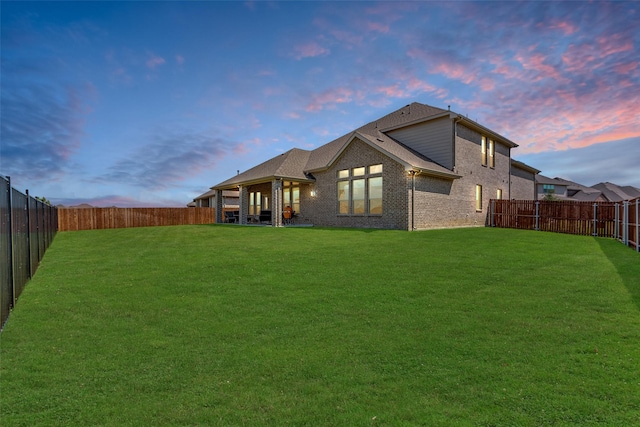 back of house at dusk featuring brick siding, a lawn, and a fenced backyard