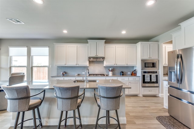 kitchen featuring under cabinet range hood, a sink, visible vents, appliances with stainless steel finishes, and light wood-type flooring