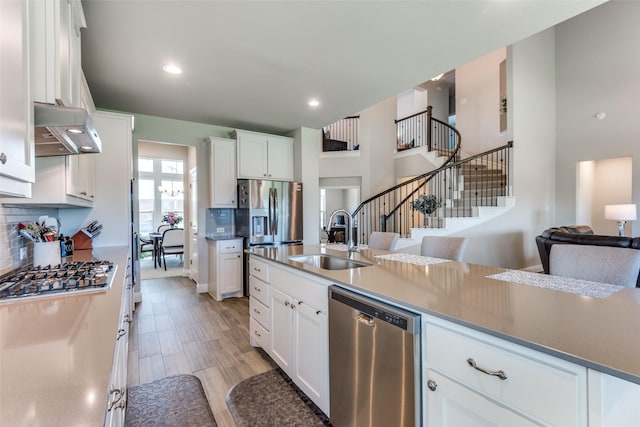 kitchen with a sink, exhaust hood, white cabinets, appliances with stainless steel finishes, and decorative backsplash