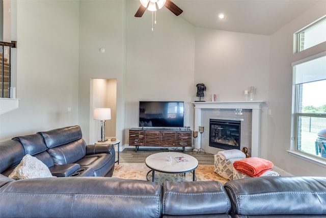 living room with wood finished floors, a ceiling fan, a towering ceiling, baseboards, and a glass covered fireplace