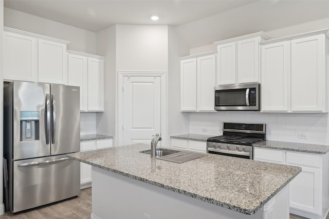 kitchen featuring light wood finished floors, backsplash, appliances with stainless steel finishes, white cabinetry, and a sink