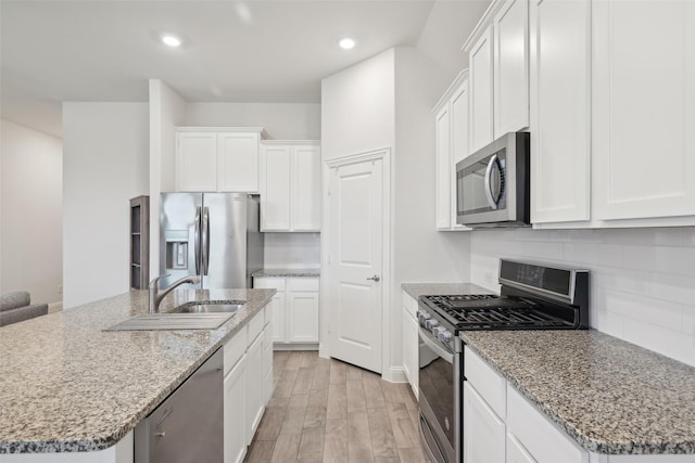 kitchen featuring stainless steel appliances, tasteful backsplash, light wood-style floors, white cabinets, and a sink